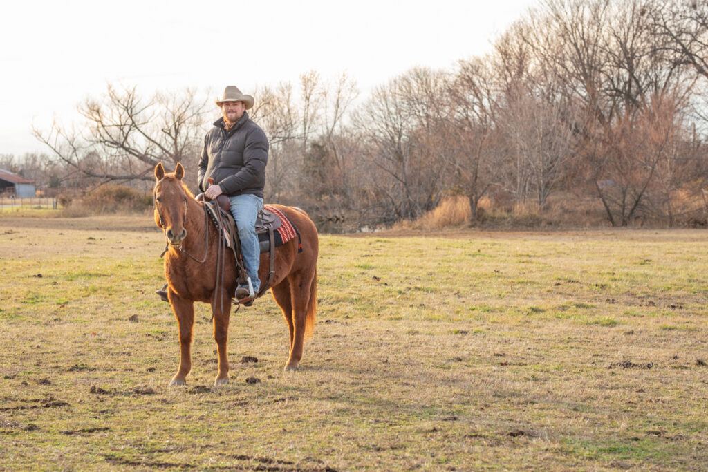 man wearing a black coat and a cowboy hat sitting on a sorrel horse wearing a western saddle