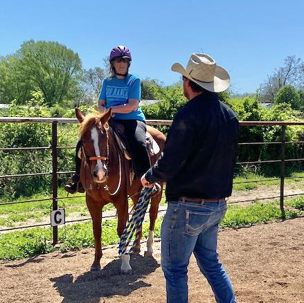 Man in black shirt and cowboy hat teaches woman on a horse how to ride