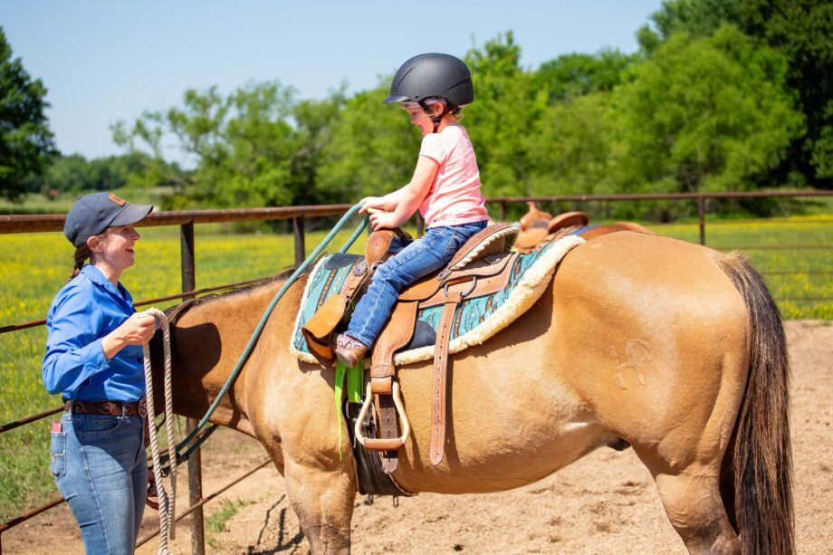 Woman gives pony ride to young girl on a brown horse