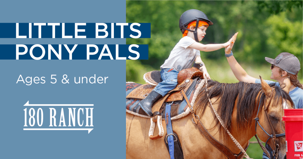 young child wearing blue jeans and a riding helmet riding a dun horse in a western saddle. The boy is giving a high five to a smiling woman on the ground.