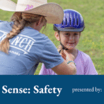 Woman in blue t shirt and cowgirl hat adjusts a purple riding helmet on a little girl in a purple t shirt